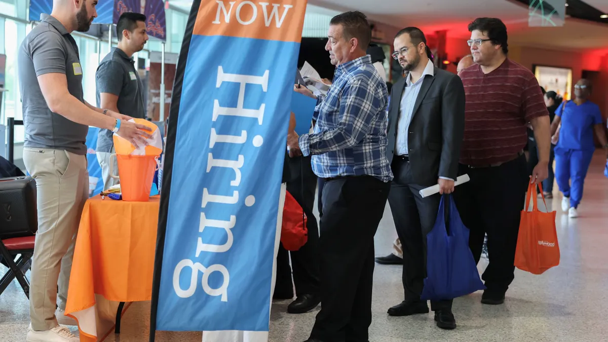 Le persone in cerca di lavoro si mettono in fila allo stand per parlare con un reclutatore durante una fiera del lavoro.